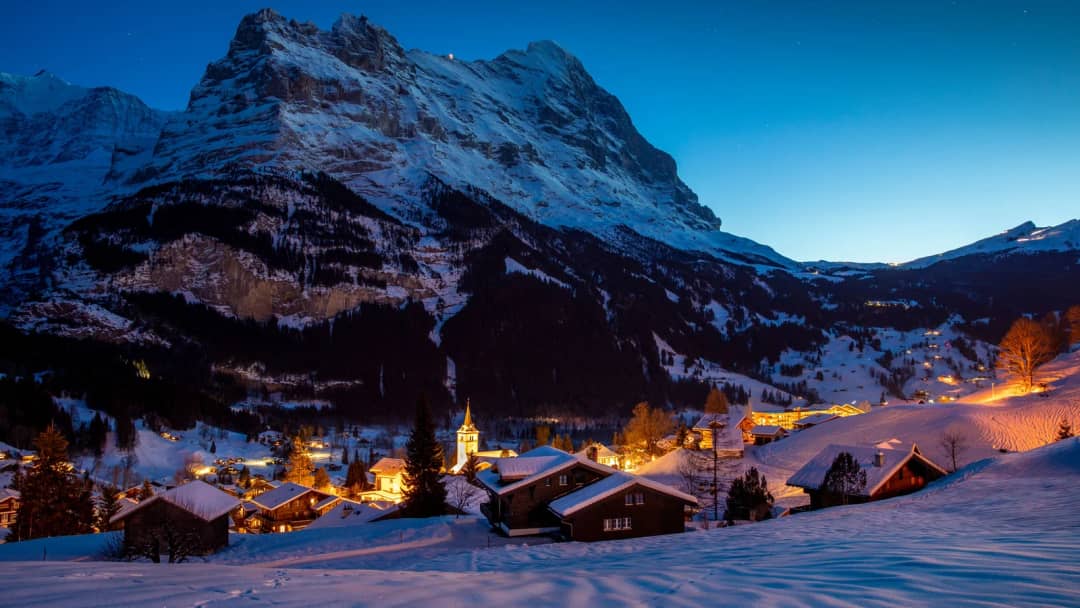 Grindelwald iluminado en la hora azul bajo la cara norte nevada del Eiger, con chalés en la nieve delante