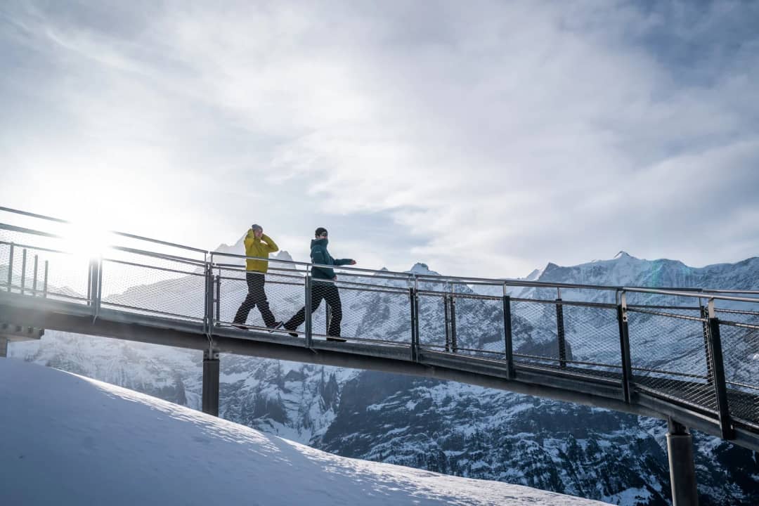 Dos caminantes en la pasarela del First Cliff Walk a 2166 m sobre Grindelwald, con cumbres nevadas detrás
