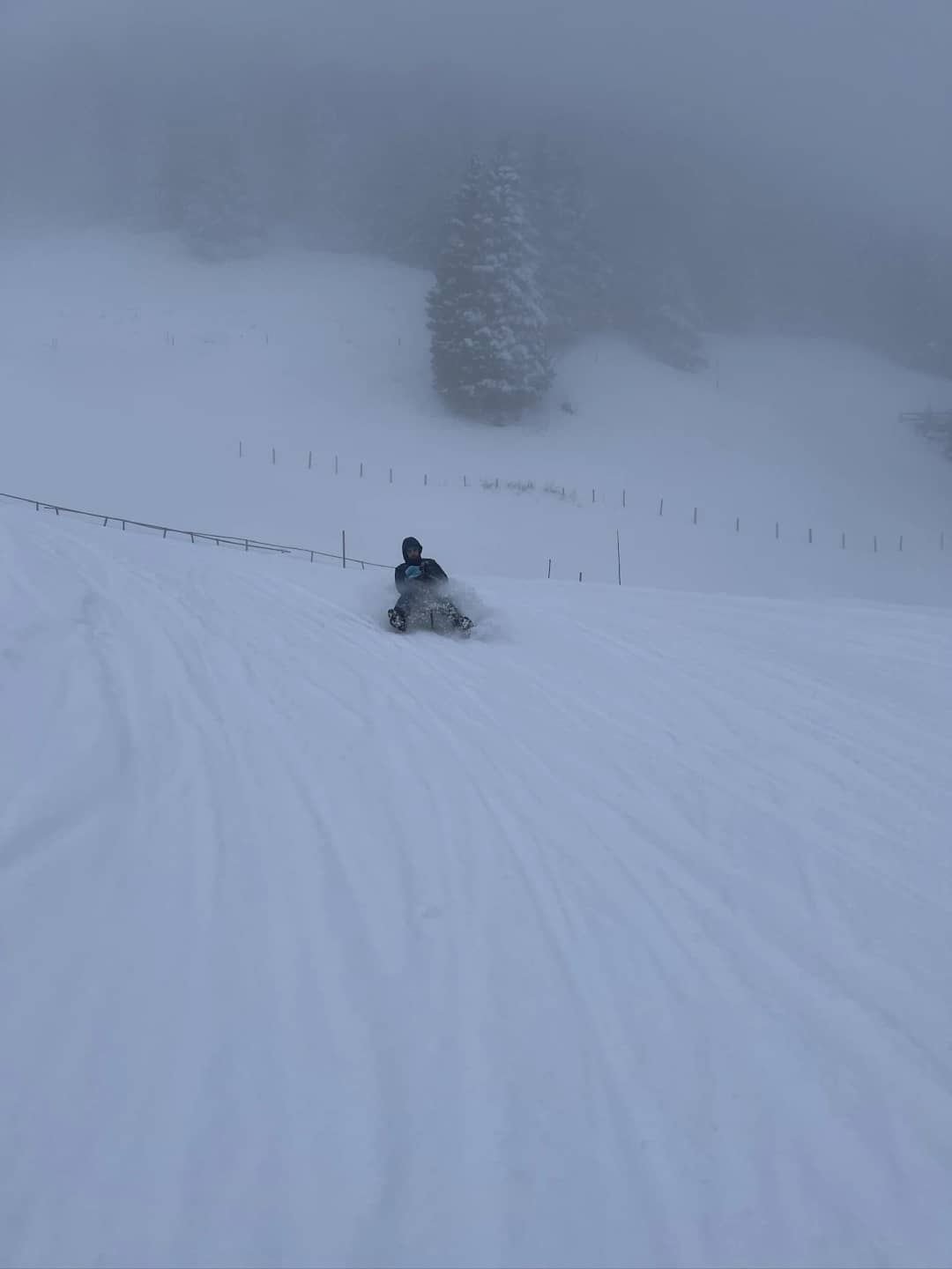 Sledder on a wooden sled heading down a wide run in thick fog above Mürren, a late March day on the sled run