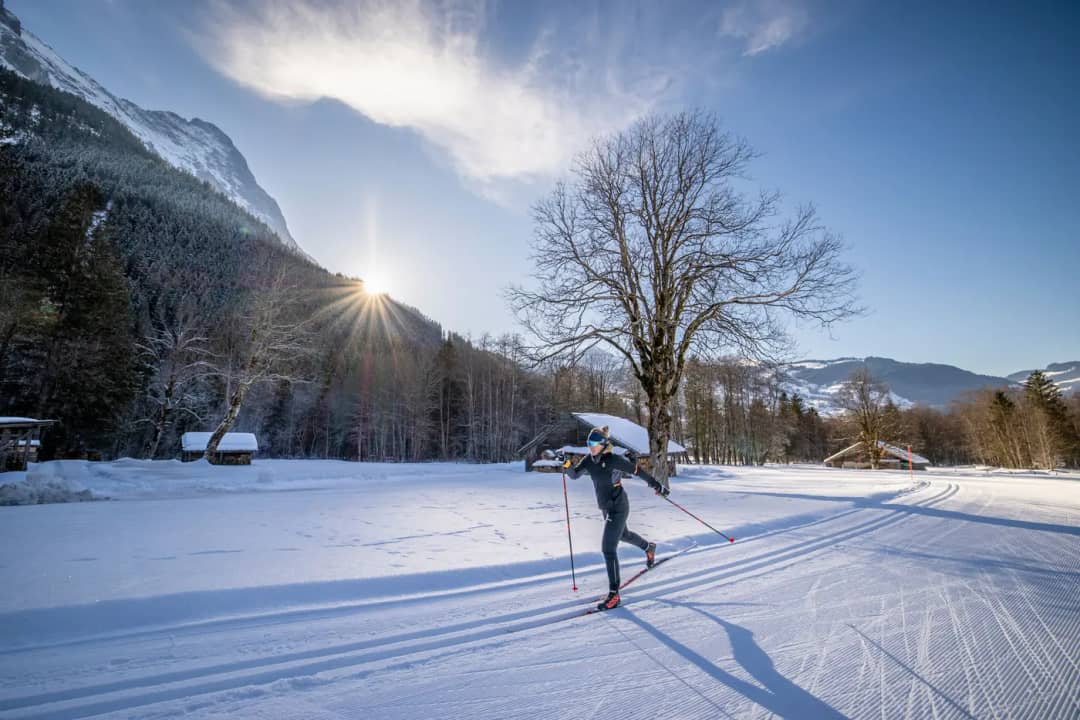Woman on cross-country skis gliding through Grindelwald in low winter light, wooden chalets behind her