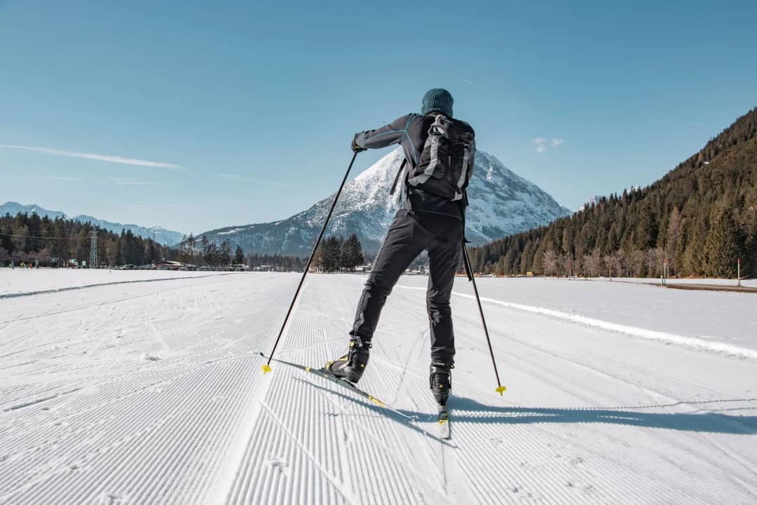 Cross-country skier on a groomed loipe in Tirol, Austria, snowy peaks behind, the trail type where Pierre fell